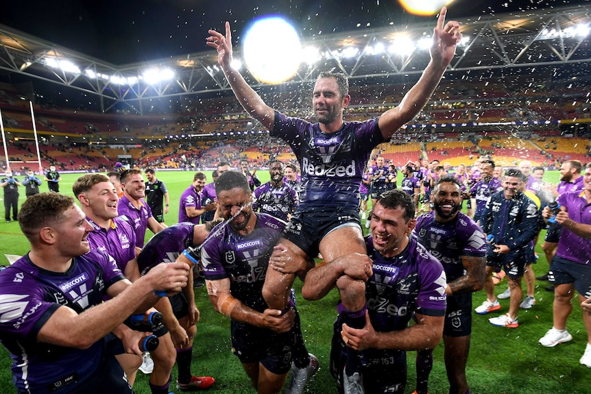 Cameron Smith sits on the shoulders of two Melbourne Storm teammates with both arms raised