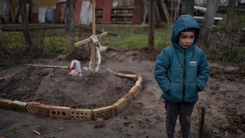 A boy standing near his mother's grave and mourning