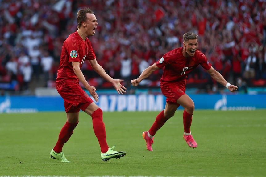 Two Danish players hold their arms out in celebration of a goal