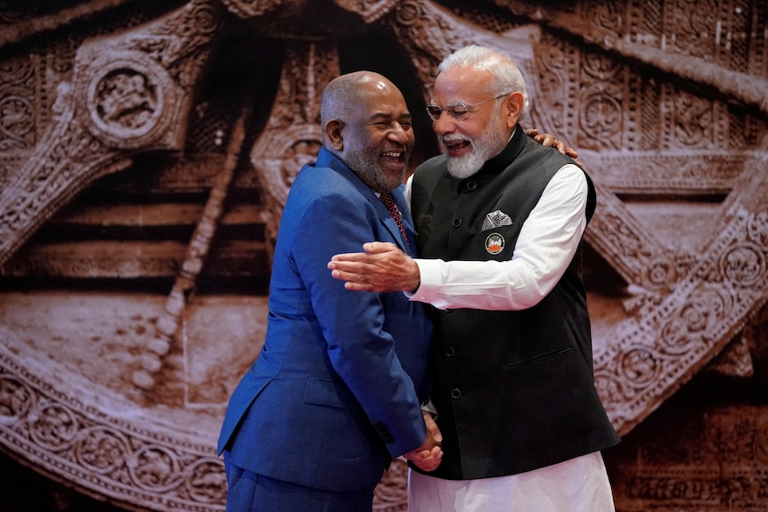Two men embrace and they are smiling.