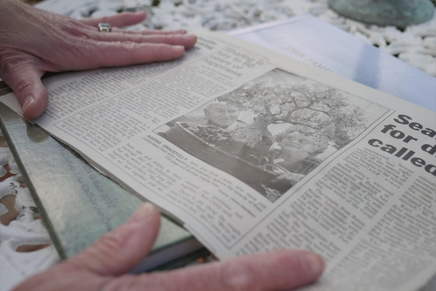 The hands of a woman holding down an old newspaper article about an elderly woman and her bonsai collection
