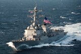 US Navy ship USS McCampbell sails through East China Sea on a clear day with a large US flag flying from the centre-deck.