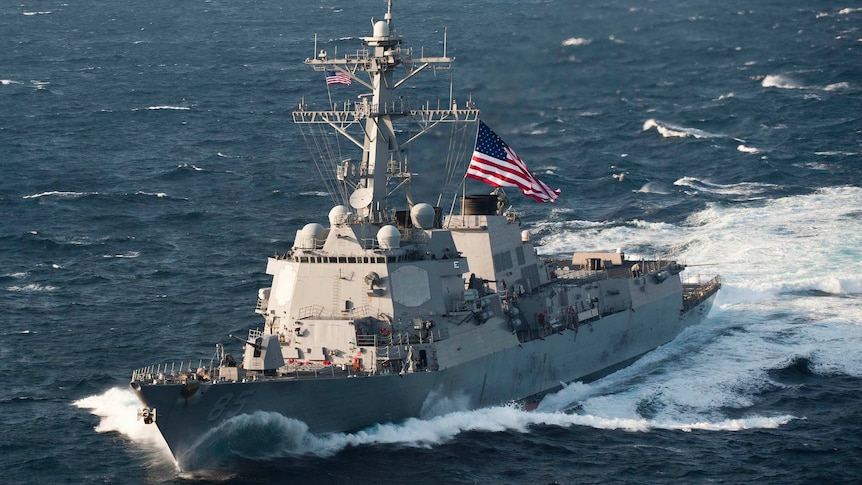 US Navy ship USS McCampbell sails through East China Sea on a clear day with a large US flag flying from the centre-deck.