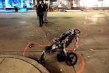 A baby stroller wrapped in Christmas tinsel with a chalk circle around it on a street with police in the background.