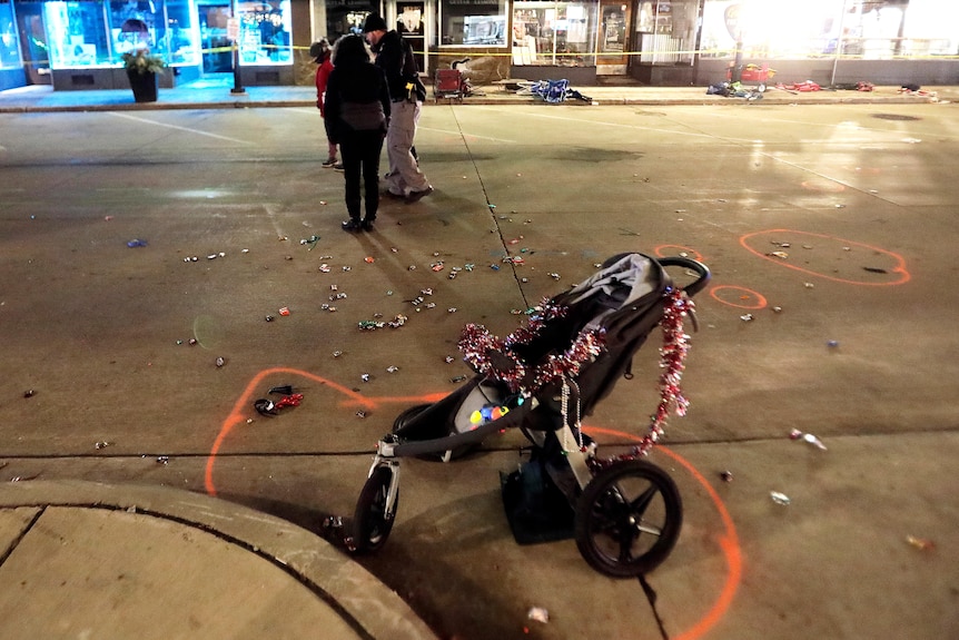 A baby stroller wrapped in Christmas tinsel with a chalk circle around it on a street with police in the background.