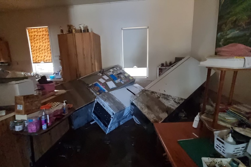 A kitchen has been turned upside down by floodwaters, fridge and appliances, mud everywhere.