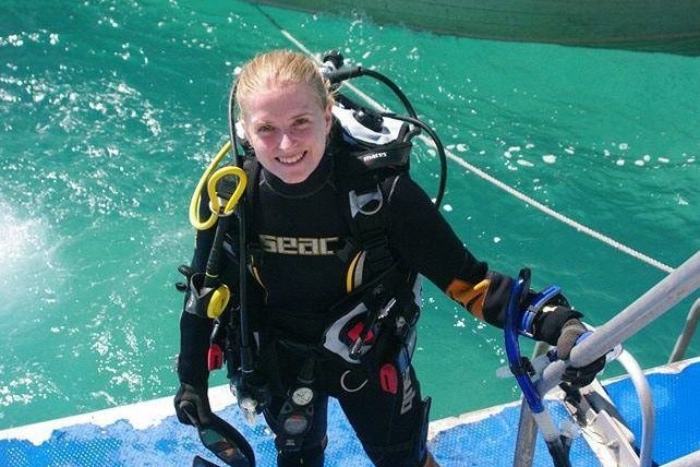 Blond hair woman smiling on he edge of a boat standing in deep sea diving gear next to aqua 