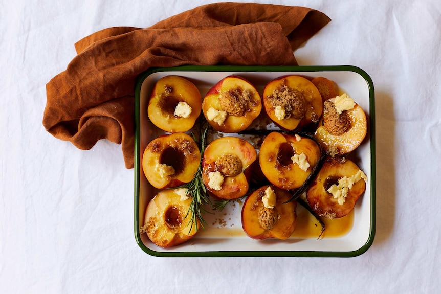 A tray of halved nectarines studded with butter, brown sugar, rosemary, ready to be roasted for a summer dessert.