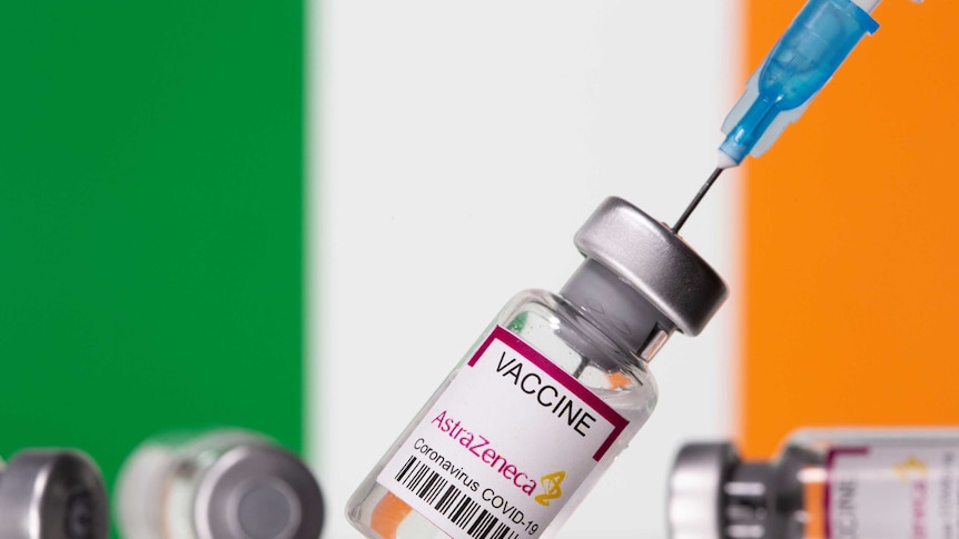 Vials labelled "Astra Zeneca COVID-19 Coronavirus Vaccine" and a syringe are seen in front of a displayed Ireland flag