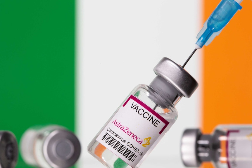 Vials labelled "Astra Zeneca COVID-19 Coronavirus Vaccine" and a syringe are seen in front of a displayed Ireland flag