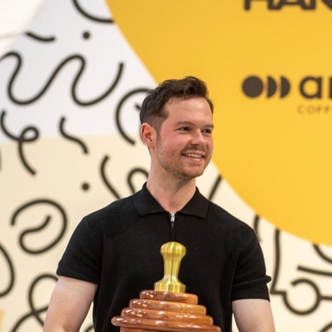 Melbourne barista Anthony Douglas smiles with a trophy with a coffee tamp on top of it
