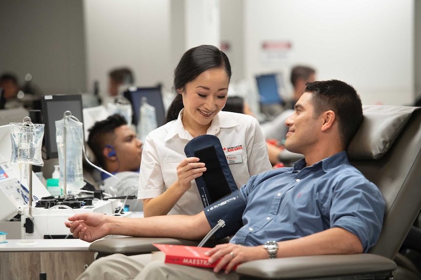 A blood donor is sitting in a chair while a nurse takes their blood pressure
