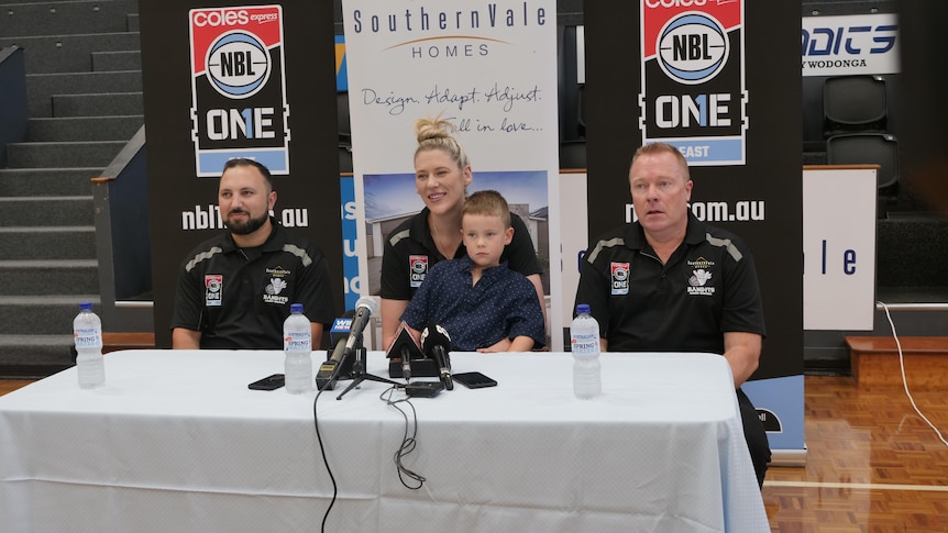 sitting at table with nbl banner in background