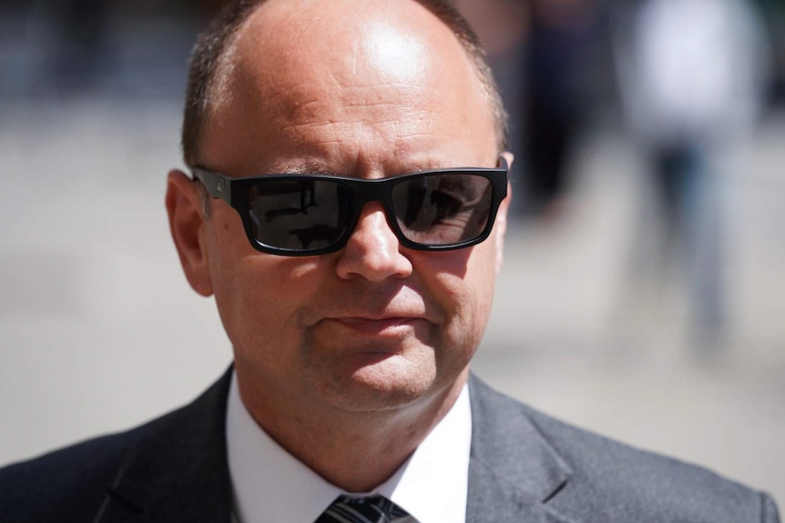 A headshot of Barry Urban wearing a suit and black sunglasses.