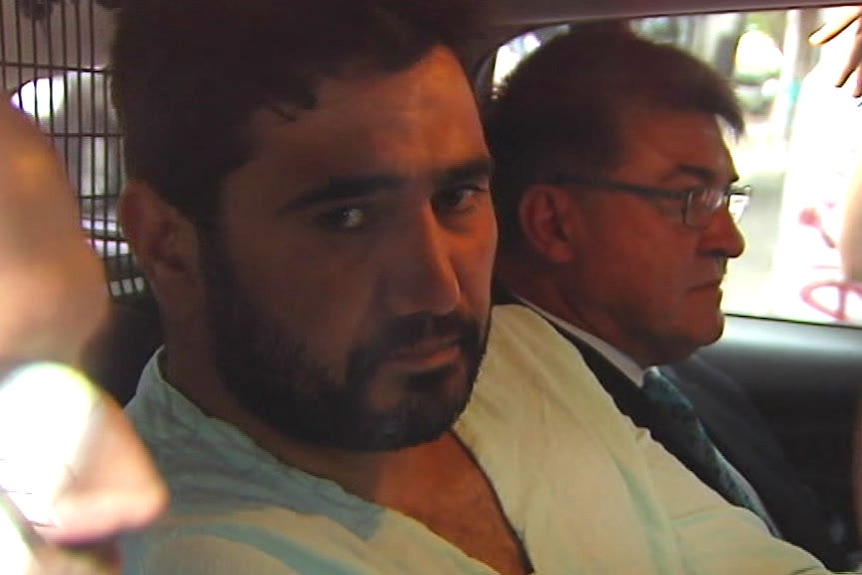 Saeed Noori is flanked by police officers in the back of a police car.