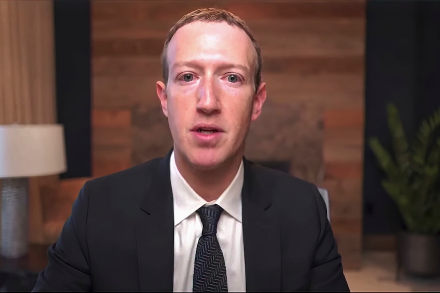 Mark Zuckerbeg dressed in a suit and jacket and with blonde hair stares at the camera.