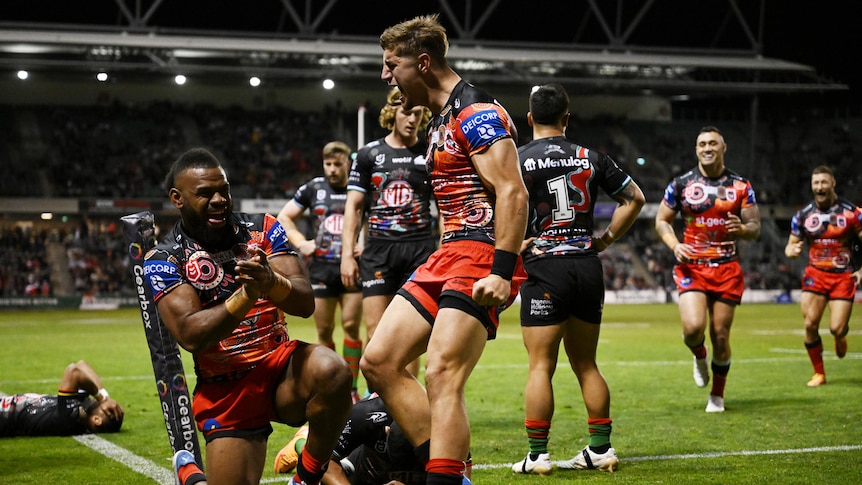 A Dragons NRL player leaps up near the corner flag with a grin on his face as his teammate runs in to congratulate him.