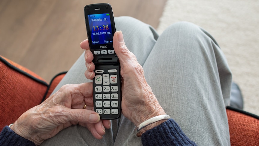 Hands of an elderly woman holding a flip phone.