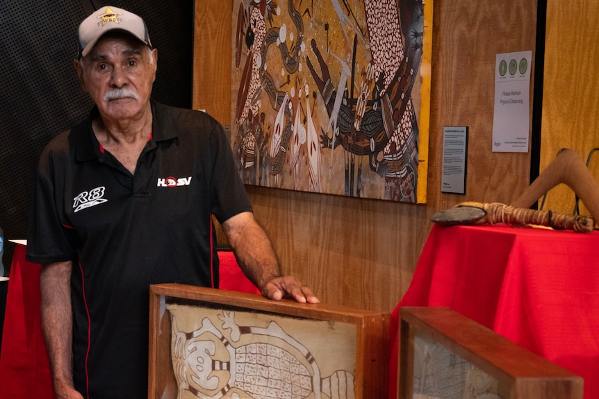 A man stands behind several framed bark paintings