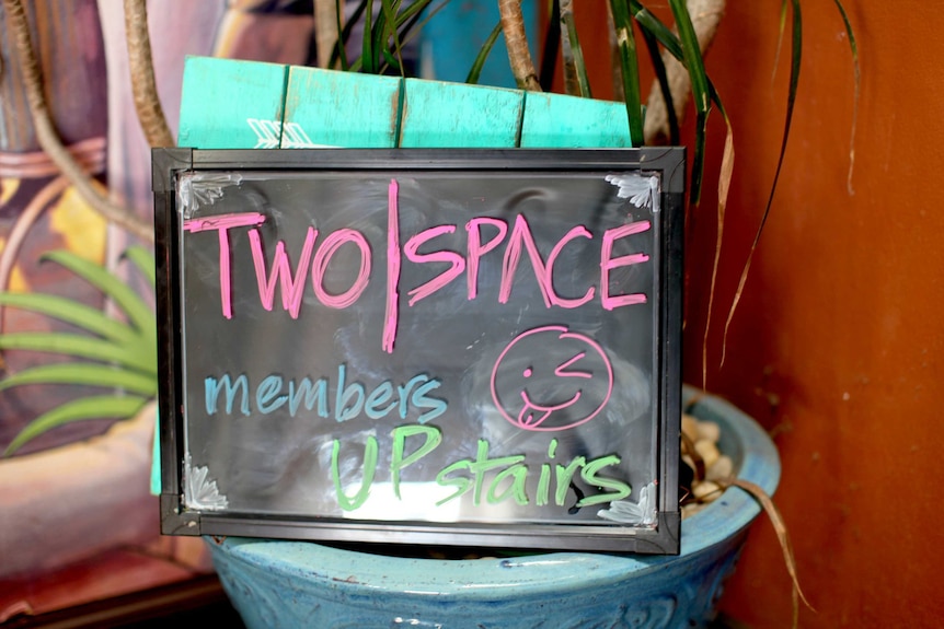 A sign says "TwoSpace members upstairs" with a smiley face drawn on