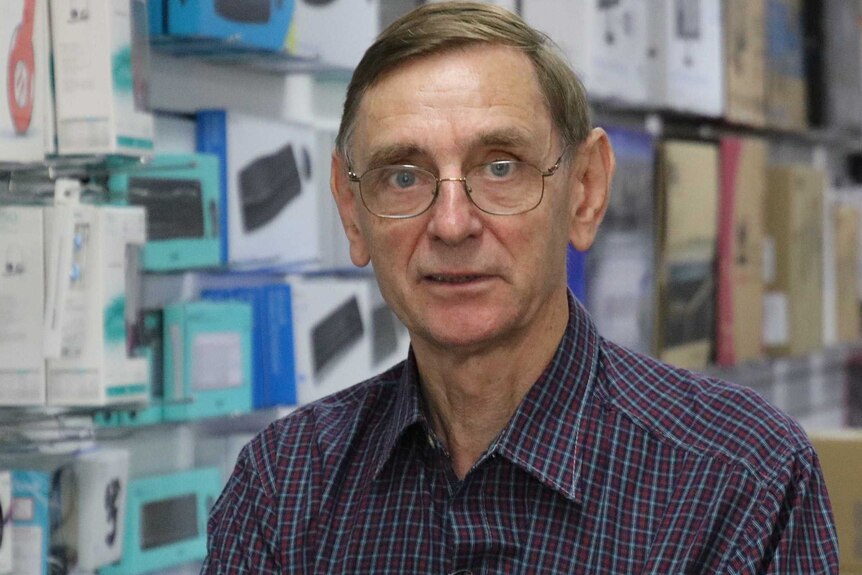 A man with a blue checked shirt stands in a computer store.