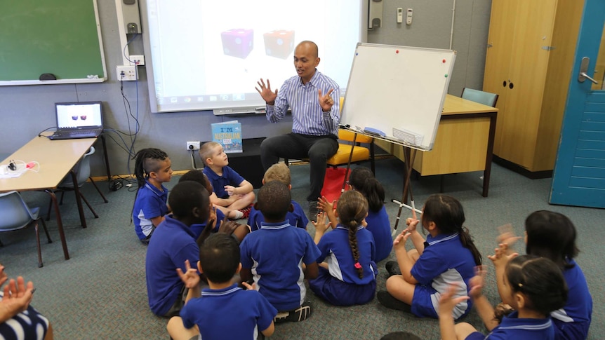 A group of students sitting on the floor around a teacher in a classroom.