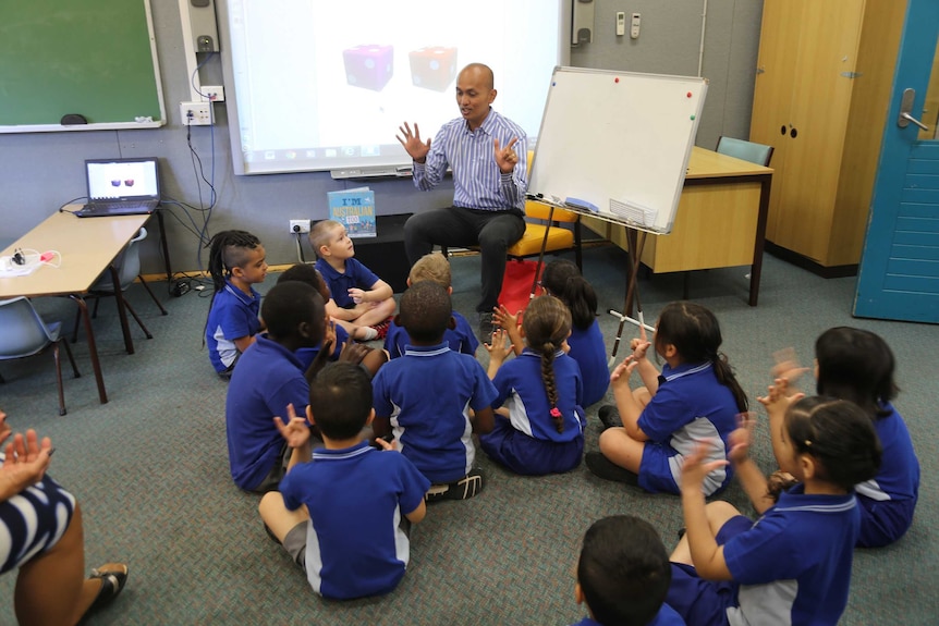 A group of students sitting on the floor around a teacher in a classroom.