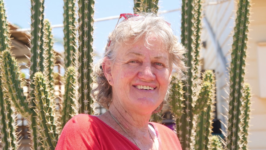 A photo of a women standing in front of a cactus. 