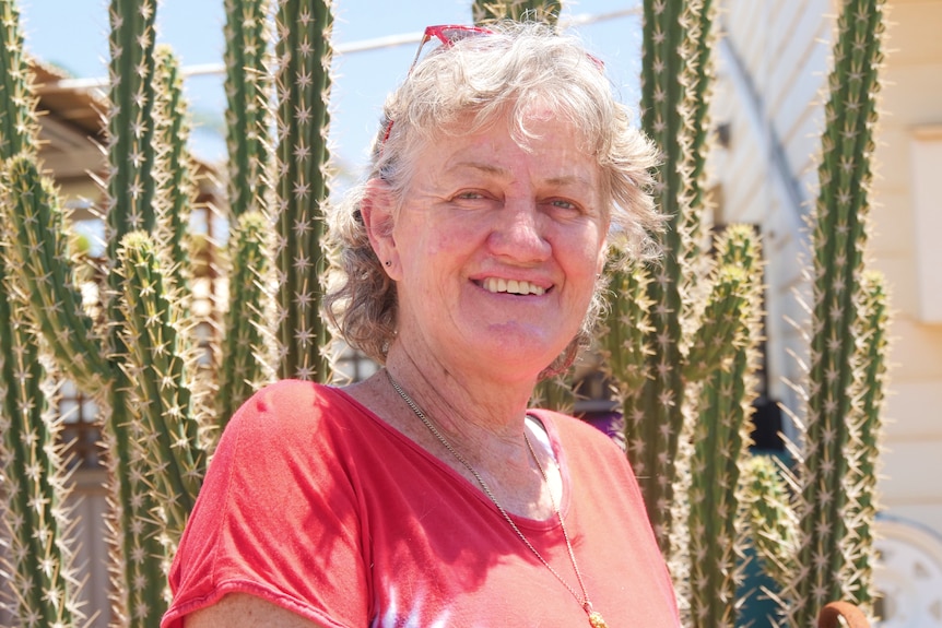 A photo of a women standing in front of a cactus. 