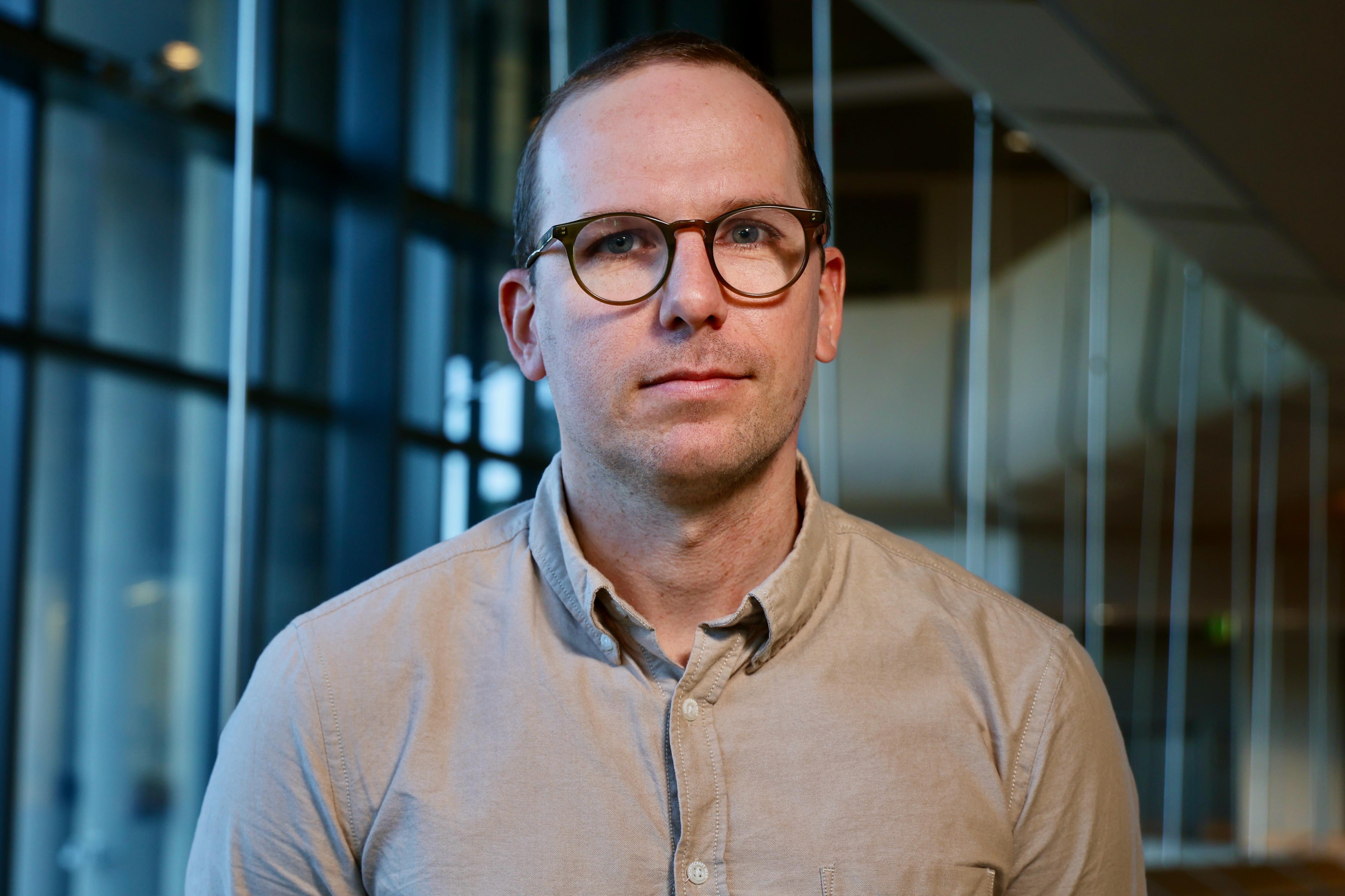 A man in a collared shirt and glasses looking into the camera.