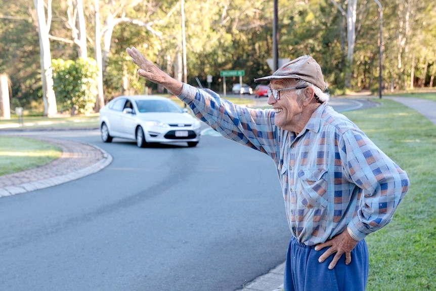 Man with a flanno shirt and hat waving to people driving around a roundabout