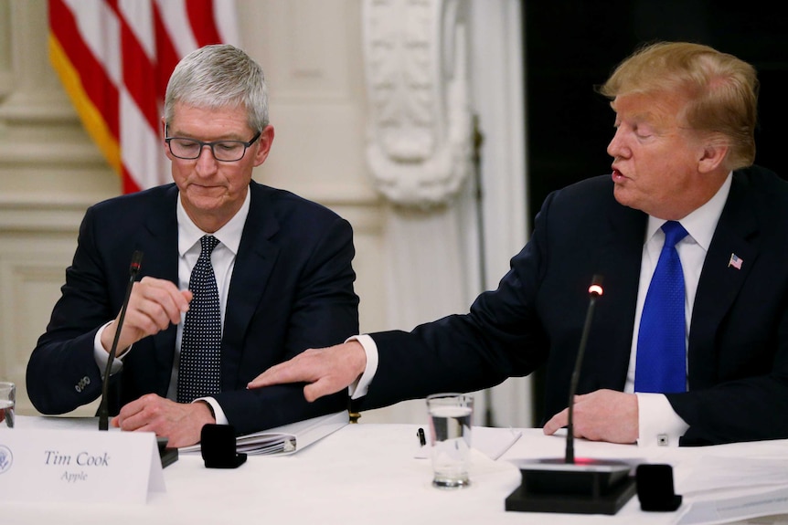US President Donald Trump holding the arm of Apple CEO Tim Cook