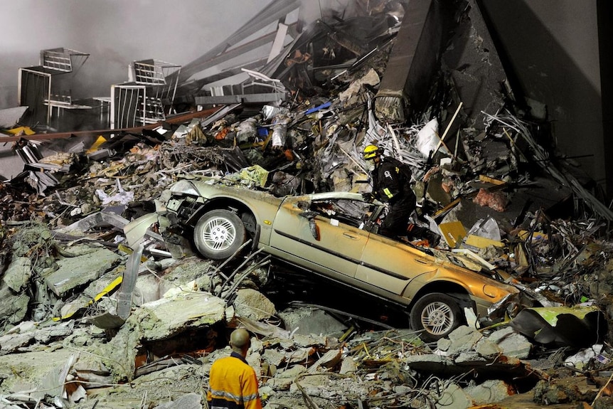 Rescue workers search through the collapsed CTV building - car wreck among the rubble (Reuters: Kyodo)