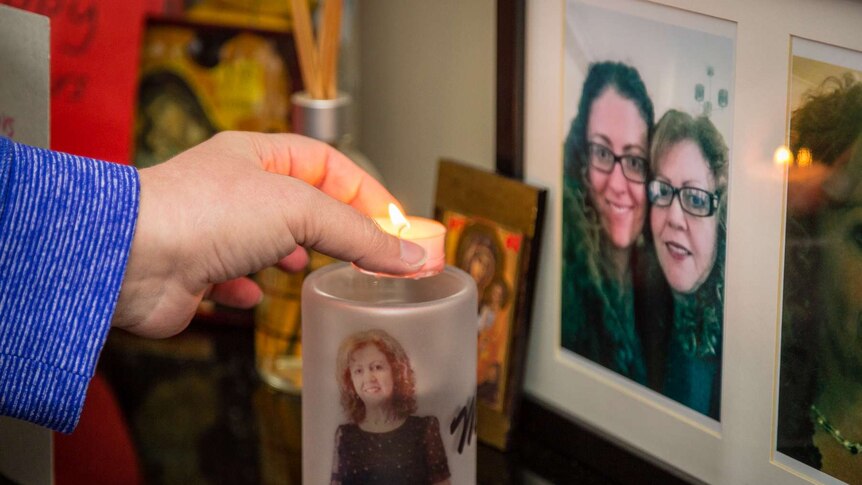 A candle lit with an image of Sonia Sofianopoulos on it next to framed family photos.