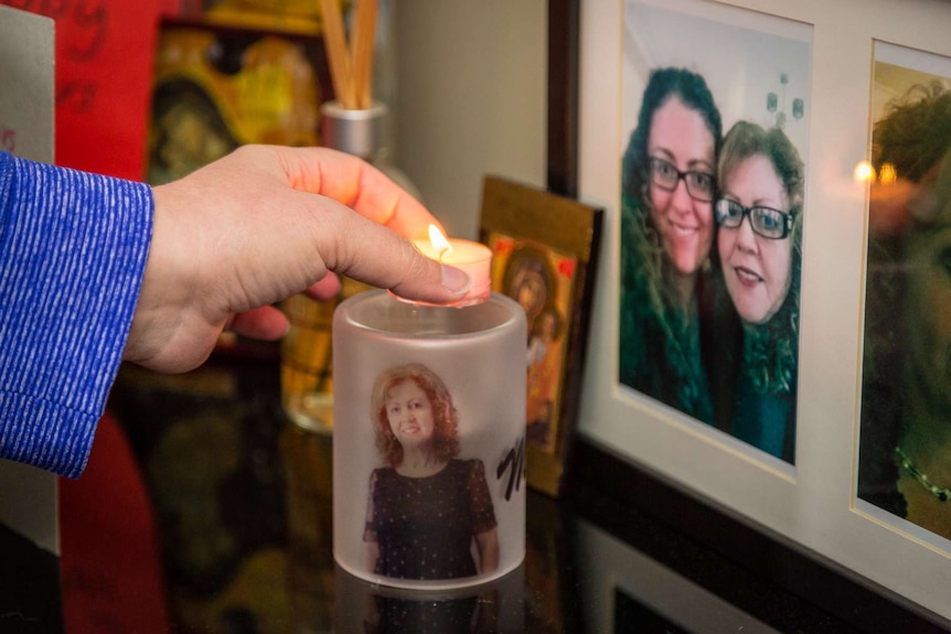 A candle lit with an image of Sonia Sofianopoulos on it next to framed family photos.