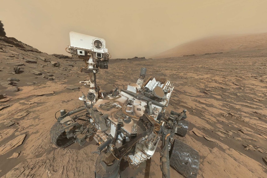 A selfie showing to full body of the Curiosity Rover on Mars, with rocks and soil around it.