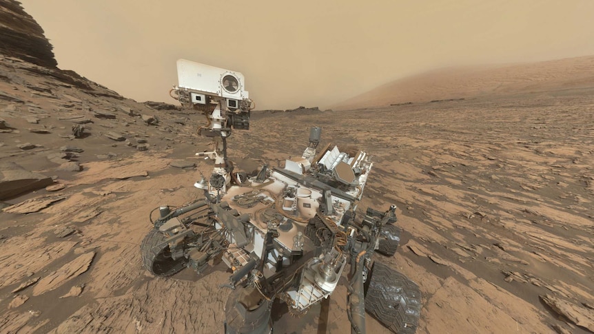 A selfie showing to full body of the Curiosity Rover on Mars, with rocks and soil around it.
