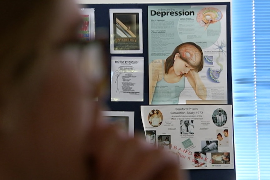 Girl blurred in the foreground sitting in classroom. Poster with the words 'depression' can be seen in background.