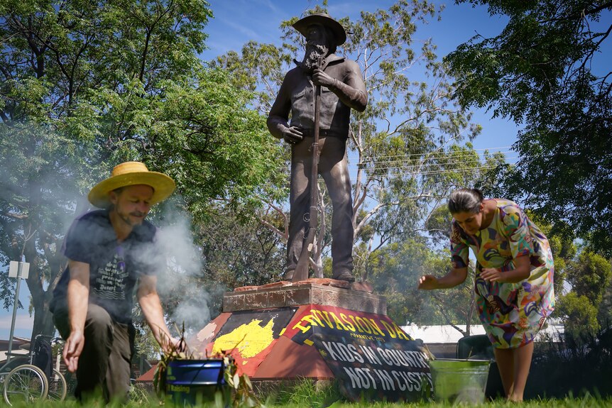 people perform a smoke ceremony in front of a statue in Alice Springs which has been painted with invasion day words