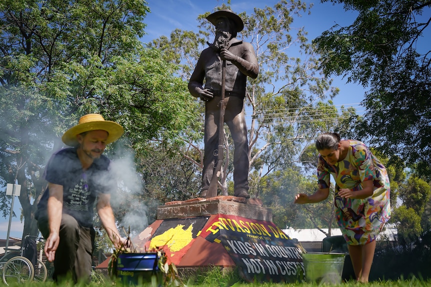 people perform a smoke ceremony in front of a statue in Alice Springs which has been painted with invasion day words