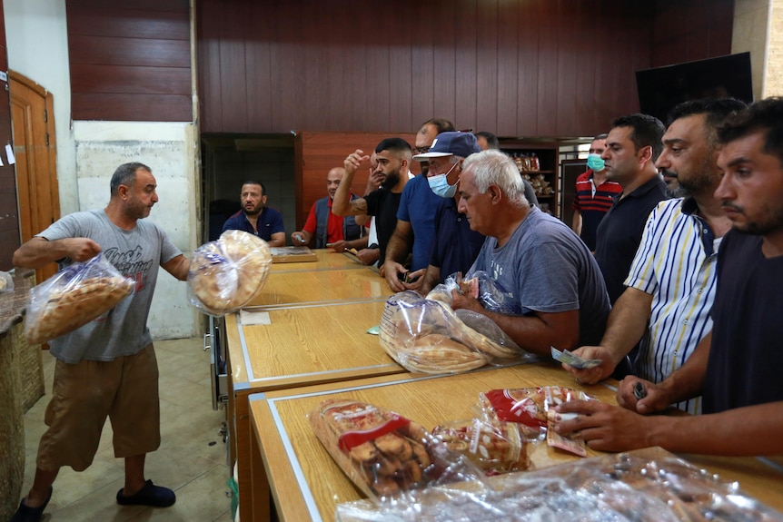 A man hands out bread to men waiting at the bakery counter.
