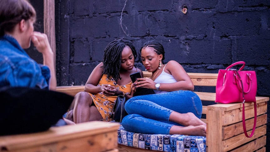 Two women sitting on timber couch looking at a phone for a story about singled and partnered friends.
