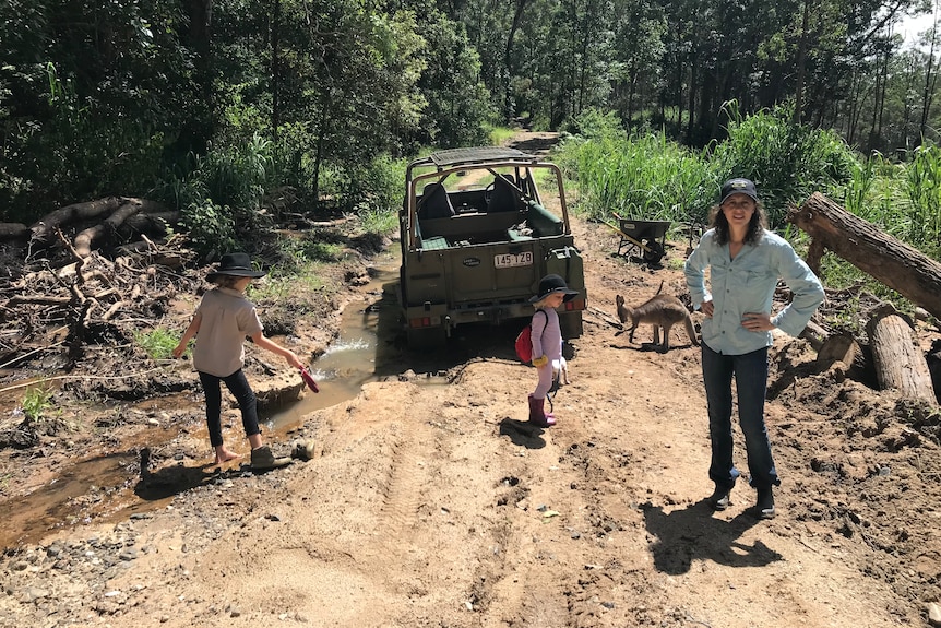 Woman standing behind four-wheel-drive with two children on dirt road