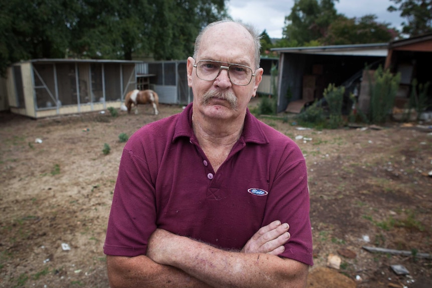 An older man wearing glasses with his arms crossed and a stern look on his face