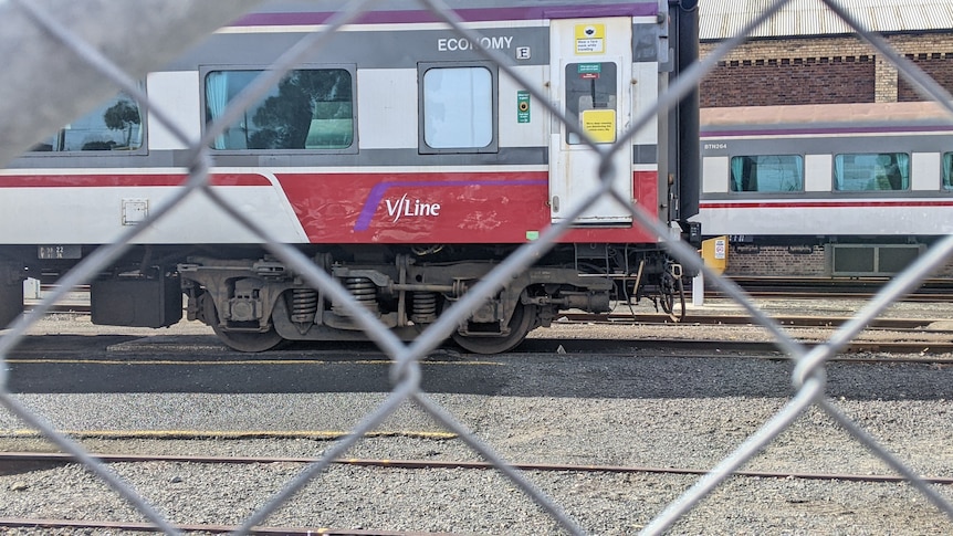 A train, seen through a fence, rolls through a yard.