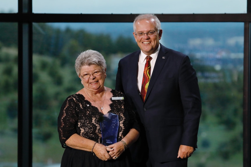 A woman smiles holding an award, next to Scott Morrison.