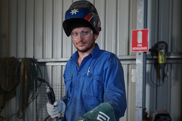 Un joven lleva un casco protector y sostiene una herramienta industrial en un taller