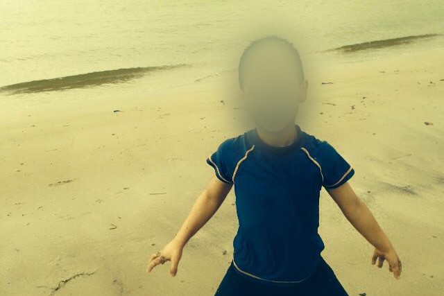 A boy stands on a beach. His face is blurred.