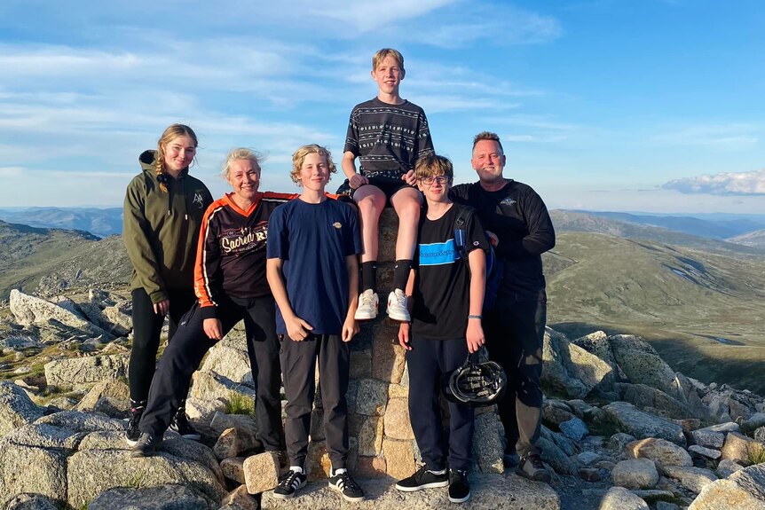 A family of two adults and four children smile on top of a mountain.