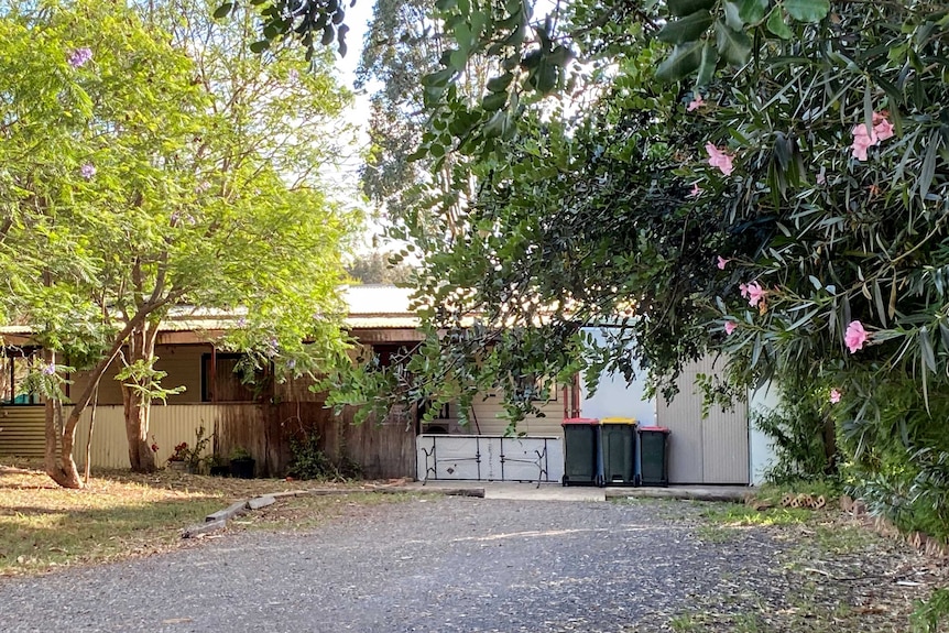Trees in foreground with asphalt driveway leading to small cream coloured unit building